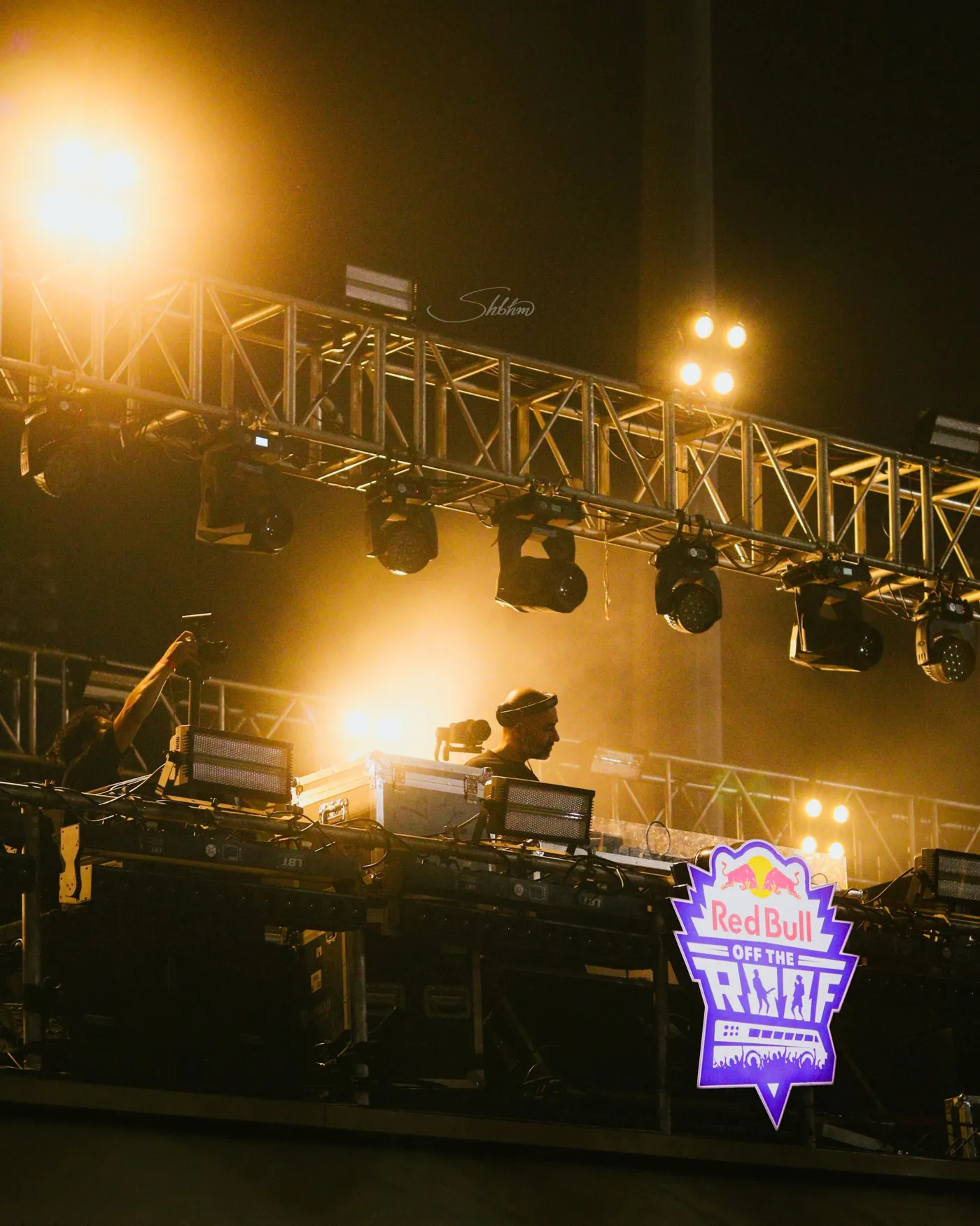 DJ beneath a lit lighting truss at a live music event