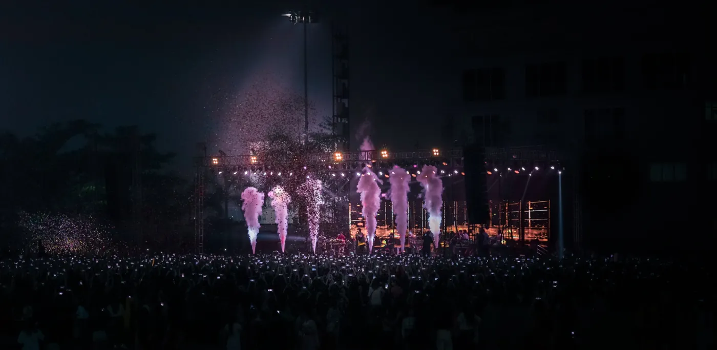 Crowd with raised phones facing a stage of cold pyro and confetti